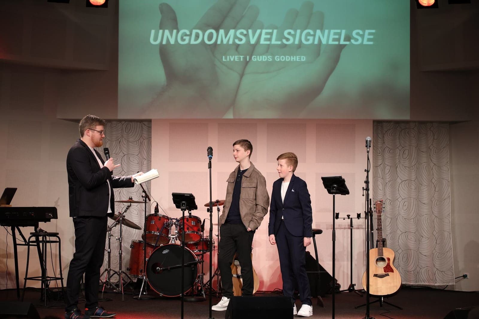Two young people standing on stage for a youth blessing while the pastor reads to them
