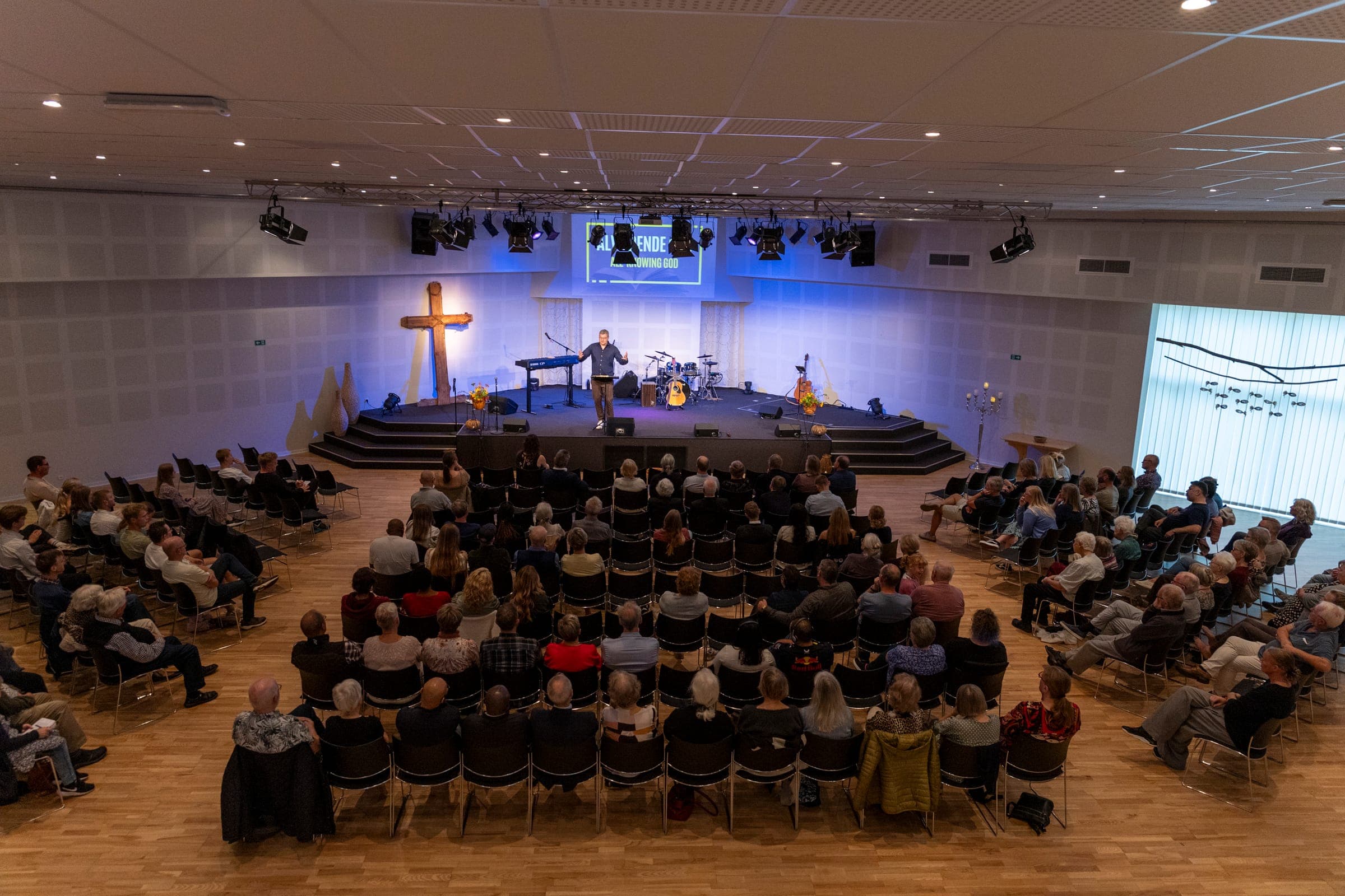 Der voll besetzte Kirchensaal während des Gottesdienstes, vorne die Bühne und das Holzkreuz
