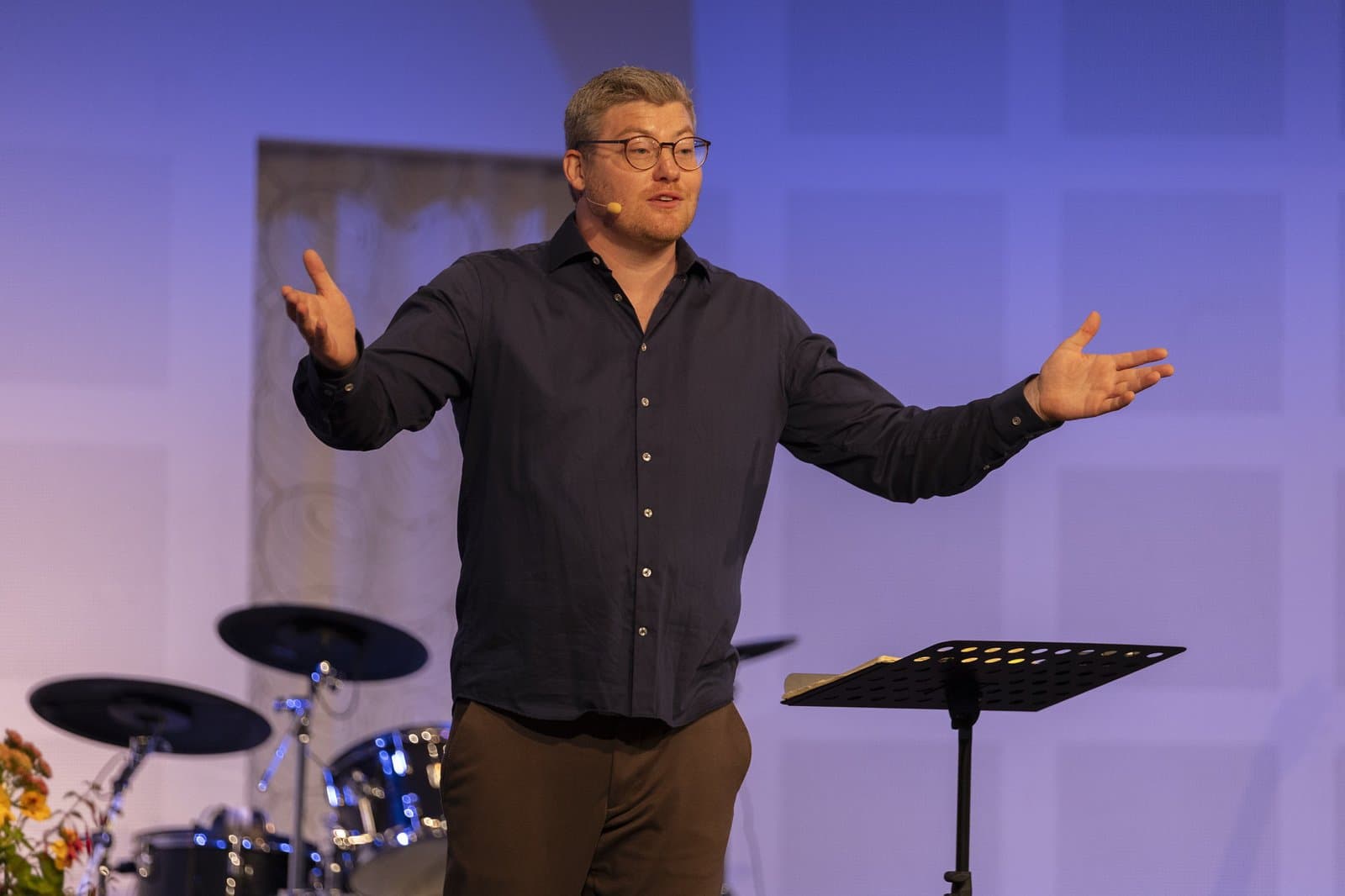 Sebastian Fredegod, Pastor der Kirken ACTS Vejle, spricht mit ausgebreiteten Armen auf der Bühne